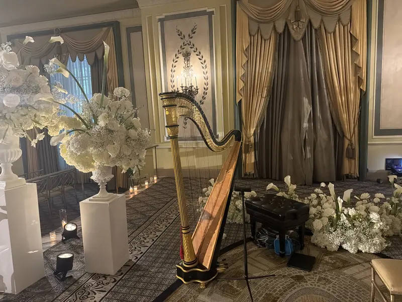 A gold pedal harp set up for a wedding ceremony among white flowers