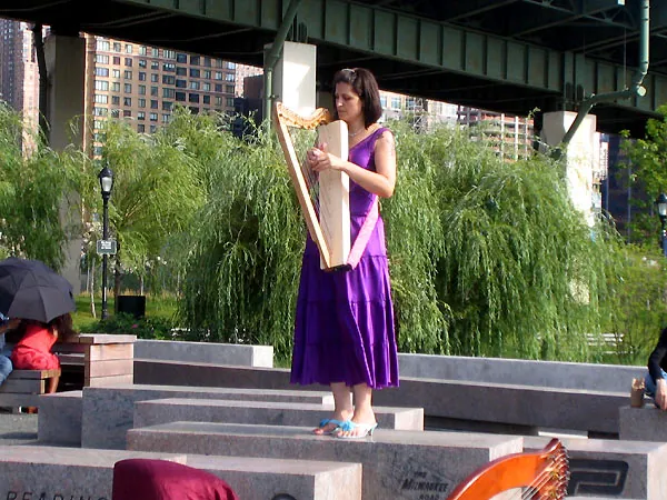 Mia playing a lever harp on a waterfront plaza