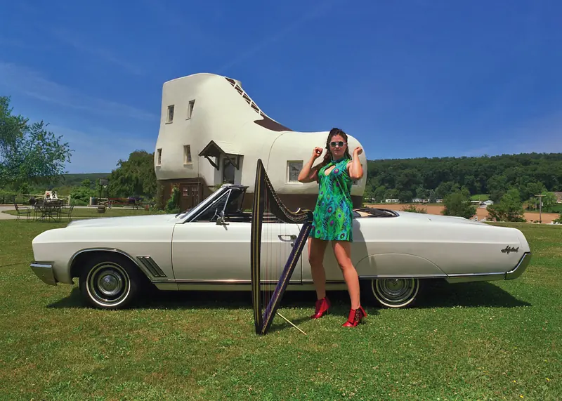 Mia in a green dress with a harp and a white convertible at the Haines Shoe House