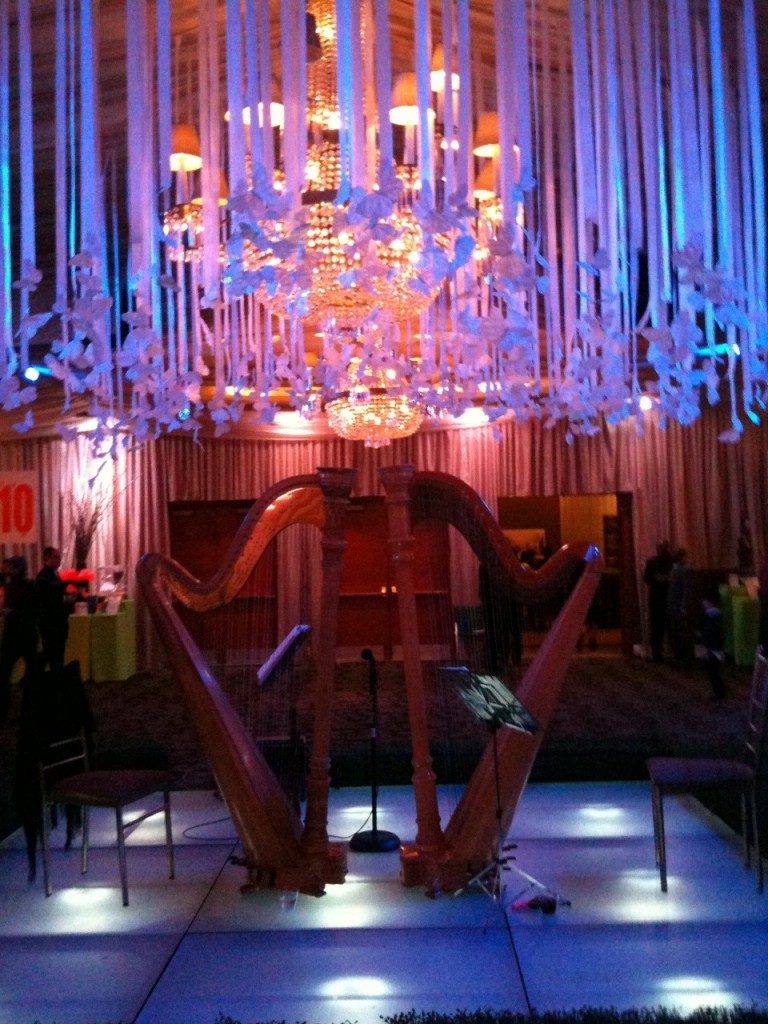Two harps set for a duet on a lit stage under a chandelier hung with ribbons